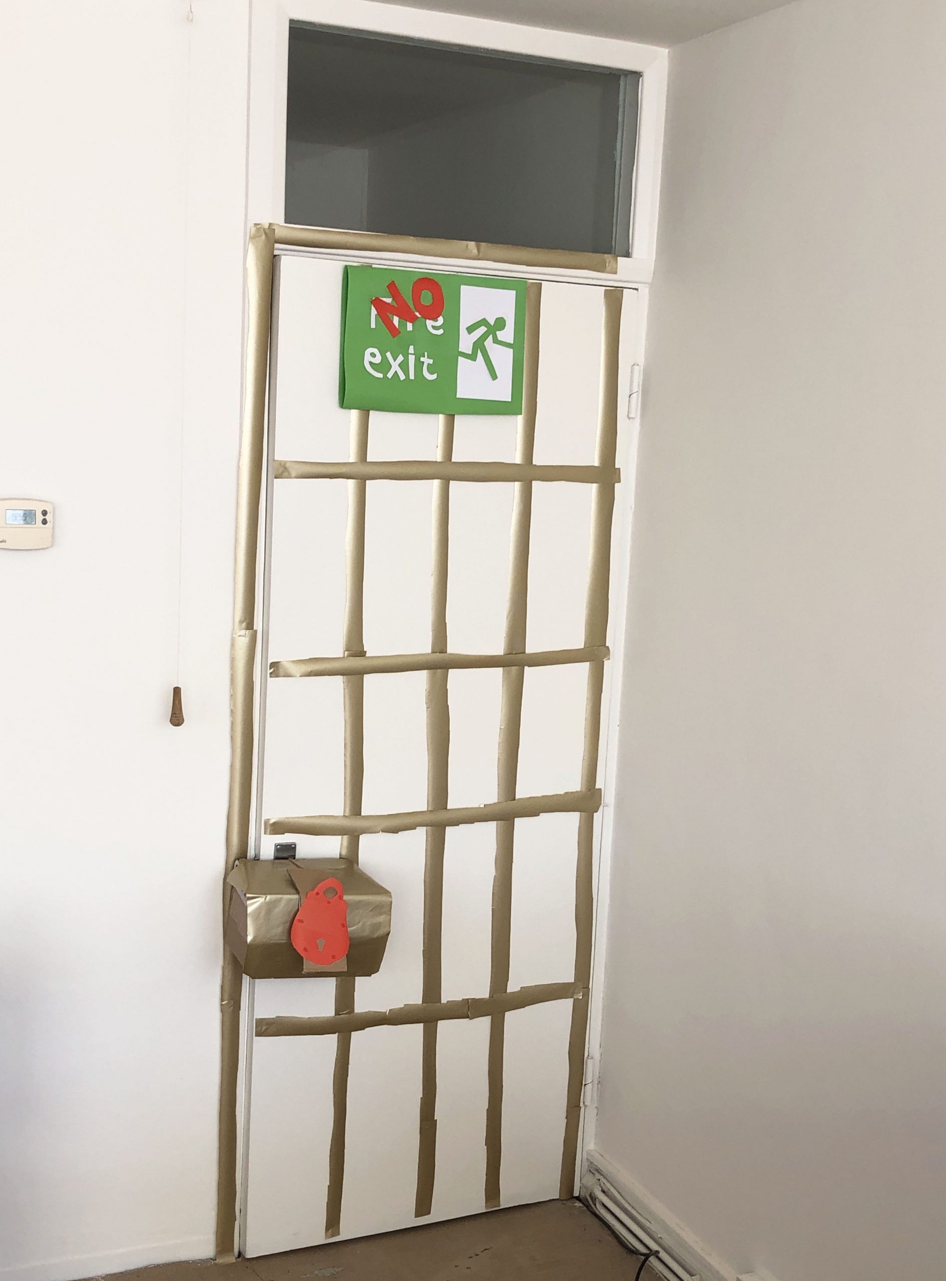 A barred and padlocked door. With a standard green Emergency Exit sign overlaid with a big red NO EXIT sign