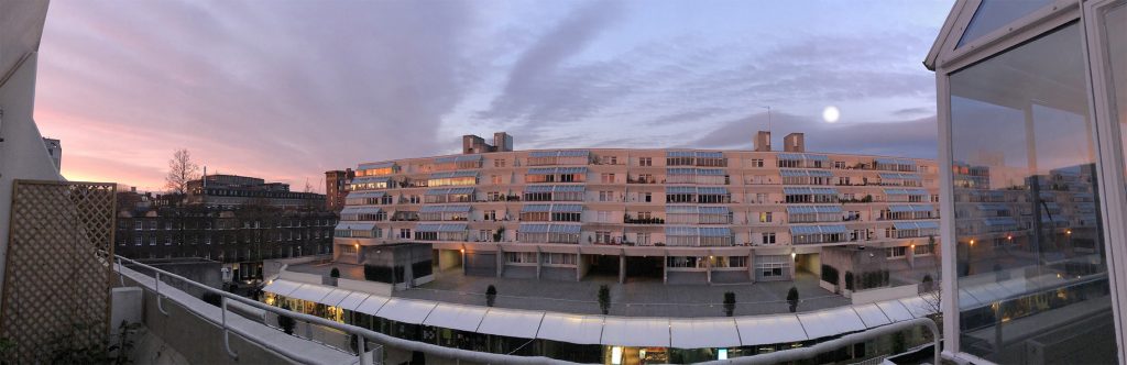Panorama showing - left to right - the pink before sunrise, then reflected orange and yellow on high up windows, then the silver-white moon before it descends